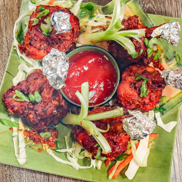 Desi Junction's red chicken lollipops with foil-wrapped bones, served with red sauce and green onions.