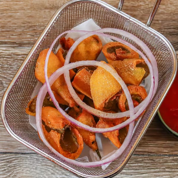 Indian chili pakoras with red onion rings in a metal basket, with red sauce on the side.