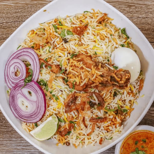 A plate of Desi Junction's chicken biryani with red onions, a lime wedge, and a hard-boiled egg.