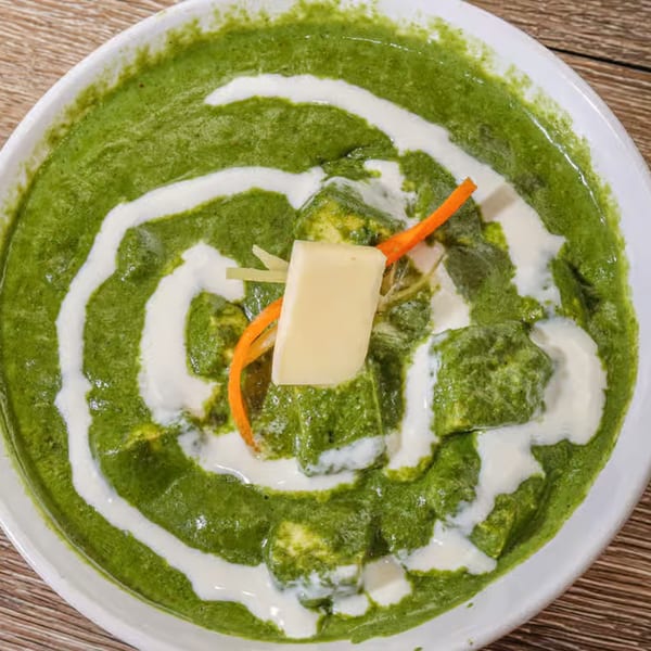 Palak Paneer, an Indian dish with green spinach curry, paneer, and cream swirls in a white bowl.