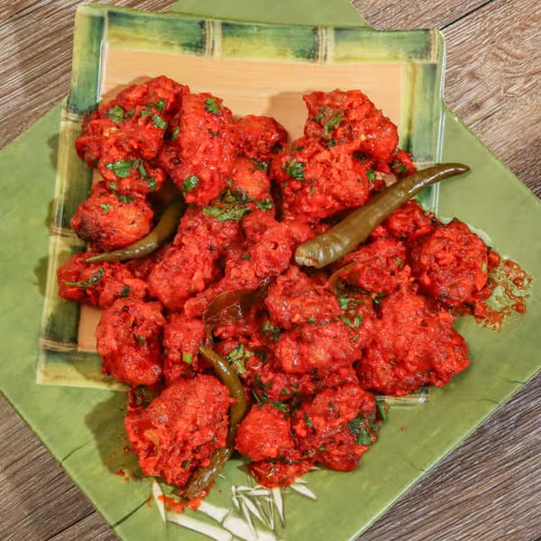 Bright red Indian Gobi Manchurian, garnished with green chilies and cilantro, on a green plate.
