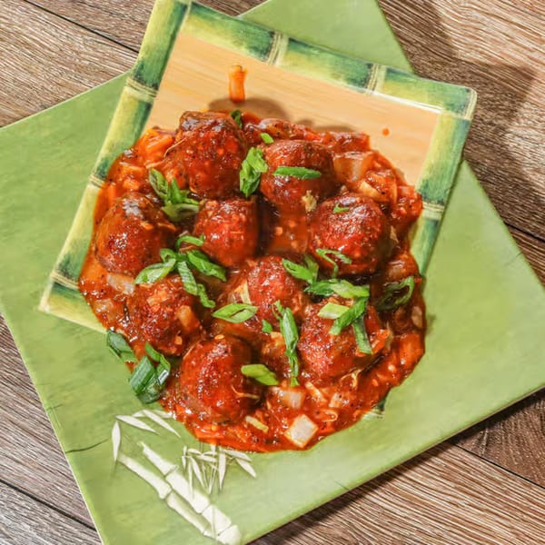 Desi Junction's Manchurian dish, featuring saucy meatballs garnished with green onions on a green plate.